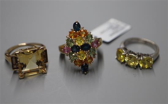 An 750 white metal three-stone ring, a multi gem-set 9ct gold dress ring and a 9ct gold three-stone topaz ring